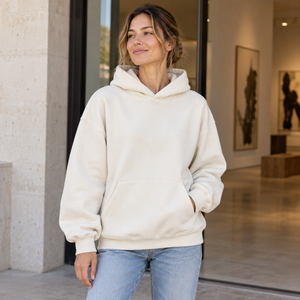 American Apparel RF498 in Bone, a stylish woman aged 29 at a contemporary gallery entrance with ivory stone and pale oak, warm natural daylight; illustrative lifestyle mockup