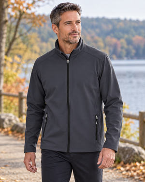 Model wearing the CORE365 88184 men's fleece bonded soft shell jacket beside a lake - Carbon