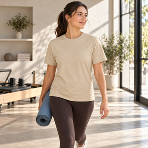 Woman wearing the CSW 24/7 Sprint S05650 T-shirt in Sand while carrying a yoga mat in a modern Pilates studio