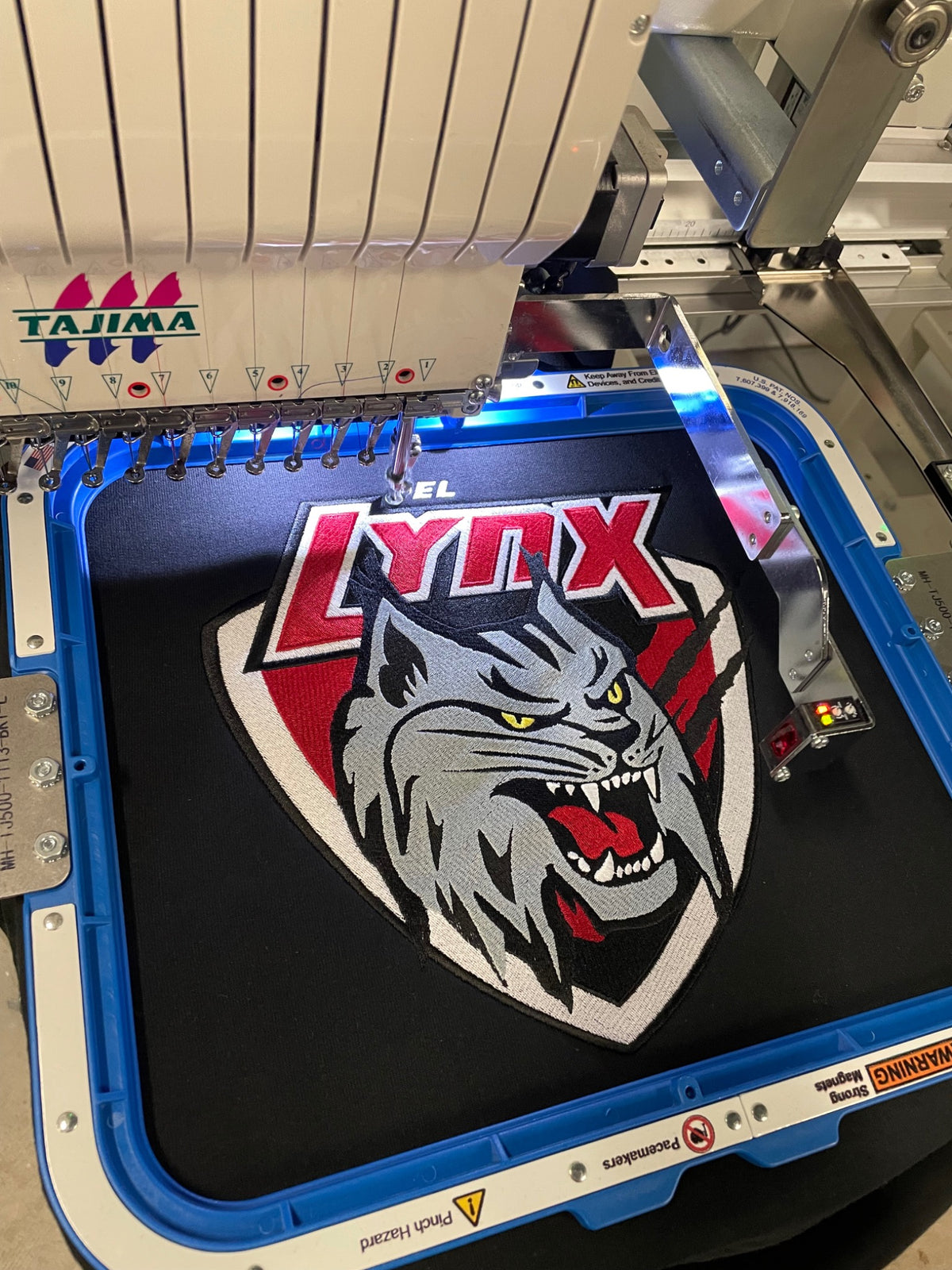 Tajima embroidery machine stitching a detailed lynx emblem