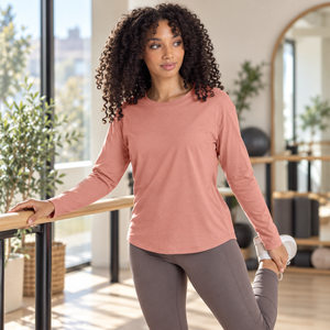 Next Level 3911 Women's Cotton Relaxed Long Sleeve Tee in Desert Pink — woman in a relaxed Pilates studio, stretching at a barre