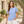 Next Level 6600 Women's CVC Relaxed Tee in Heather Columbia Blue — woman beside a sunlit stone courtyard and an olive tree