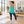 Next Level 6733 Women's Triblend Racerback Tank in Tahiti Blue — woman doing an easy standing stretch in a bright Pilates studio, no mat pose