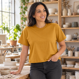 Next Level 7610 Women's Heavyweight Boxy Tee in Antique Gold — woman at an airy ceramics workshop with shelves of handmade objects